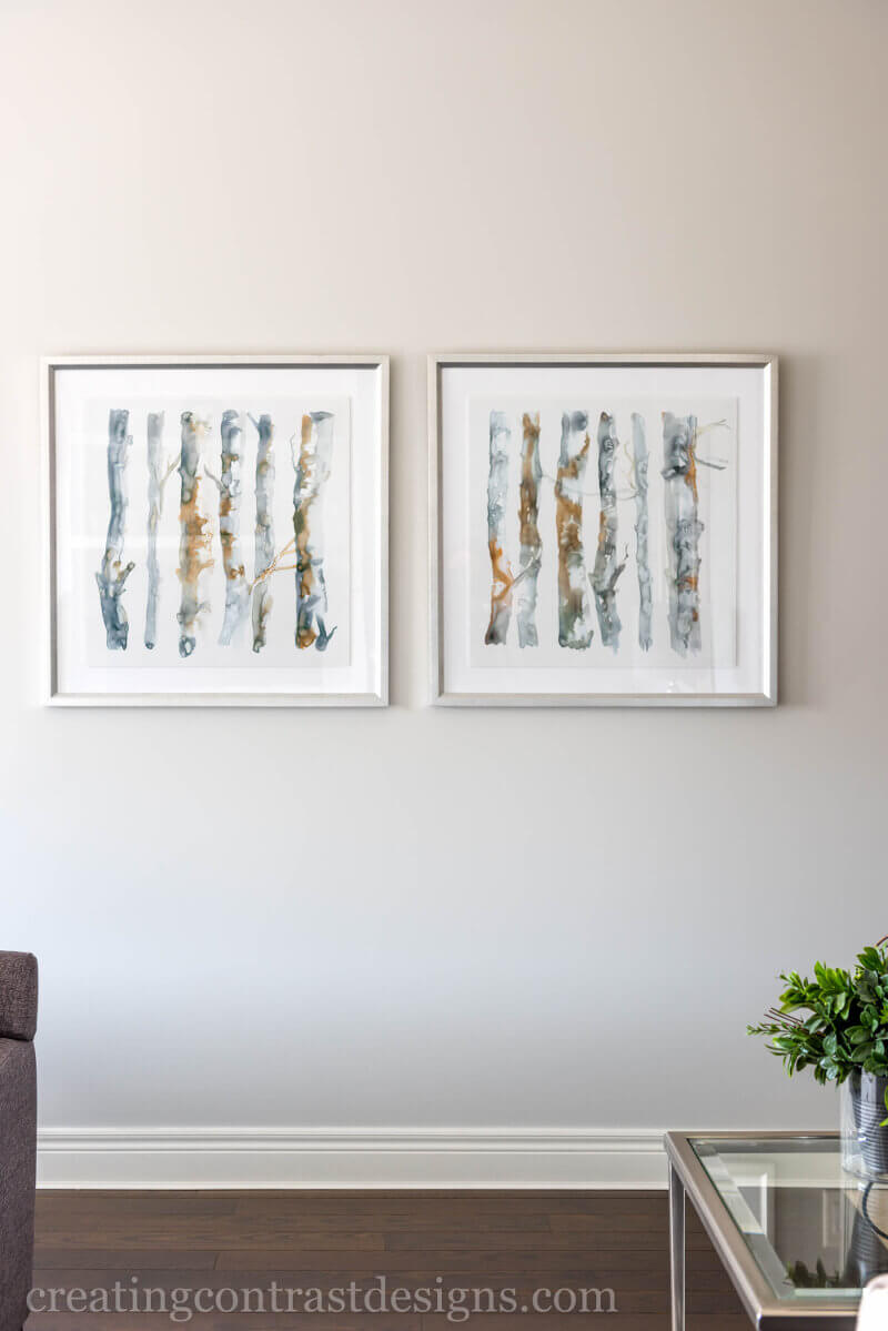 Gallery Art Wall With Watercolour Tree Paintings And Dark Hardwood Flooring With White Trim And Glass Coffee Table In Traditional Living Room