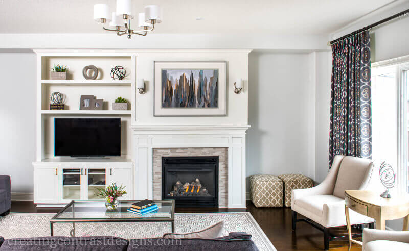 White Custom Cabinetry With Art Wall Over Fireplace And Built In Tv And Custom Fabric On Side Chair In Elegant Living Room