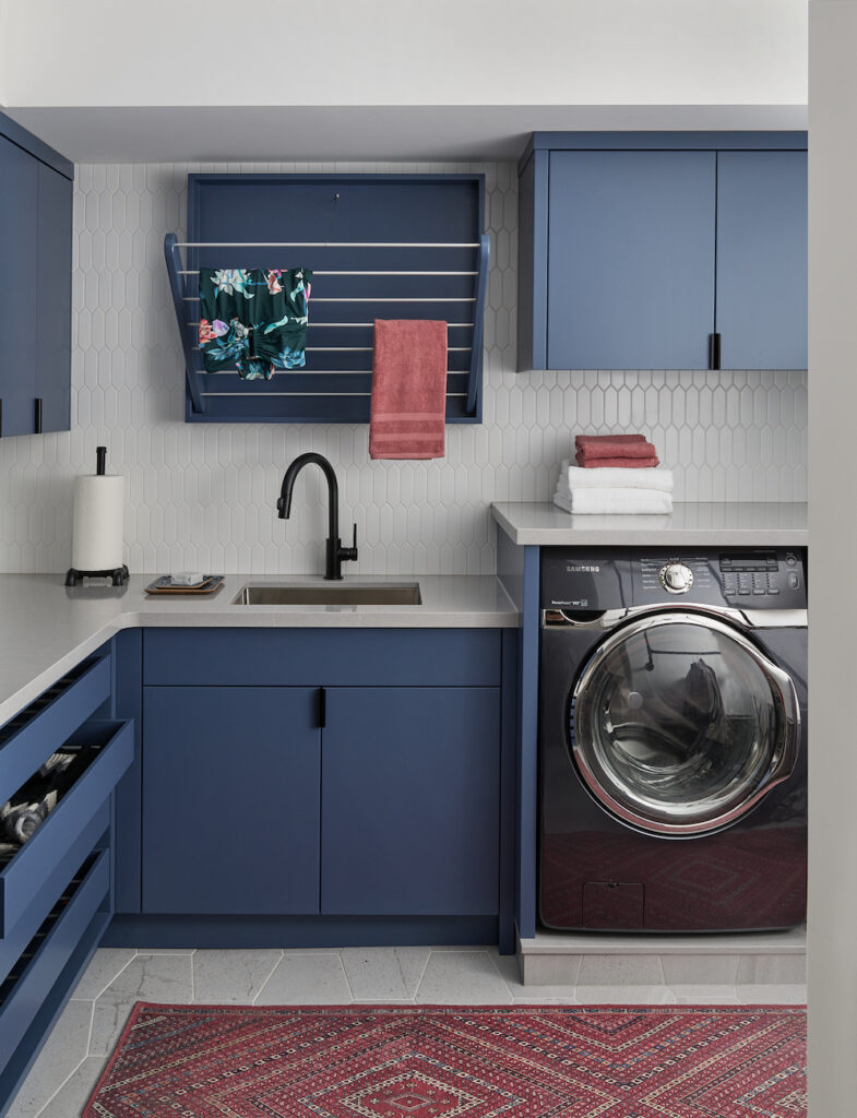 Organized Laundry Room Blue Cabinets Pull Down Dry Rack Black Hardware Black Faucet Picket Fence Tile