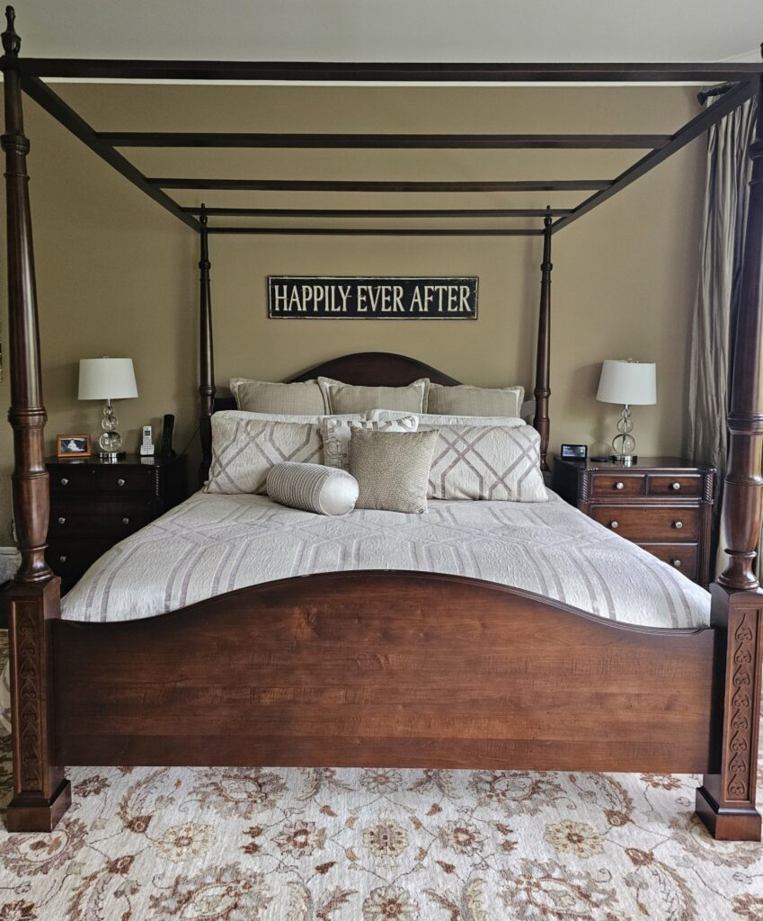 Before image of traditional four-poster bed with cream bedding and “Happily Ever After” sign above, flanked by dark nightstands on beige walls, Burlington project by clairejefford.