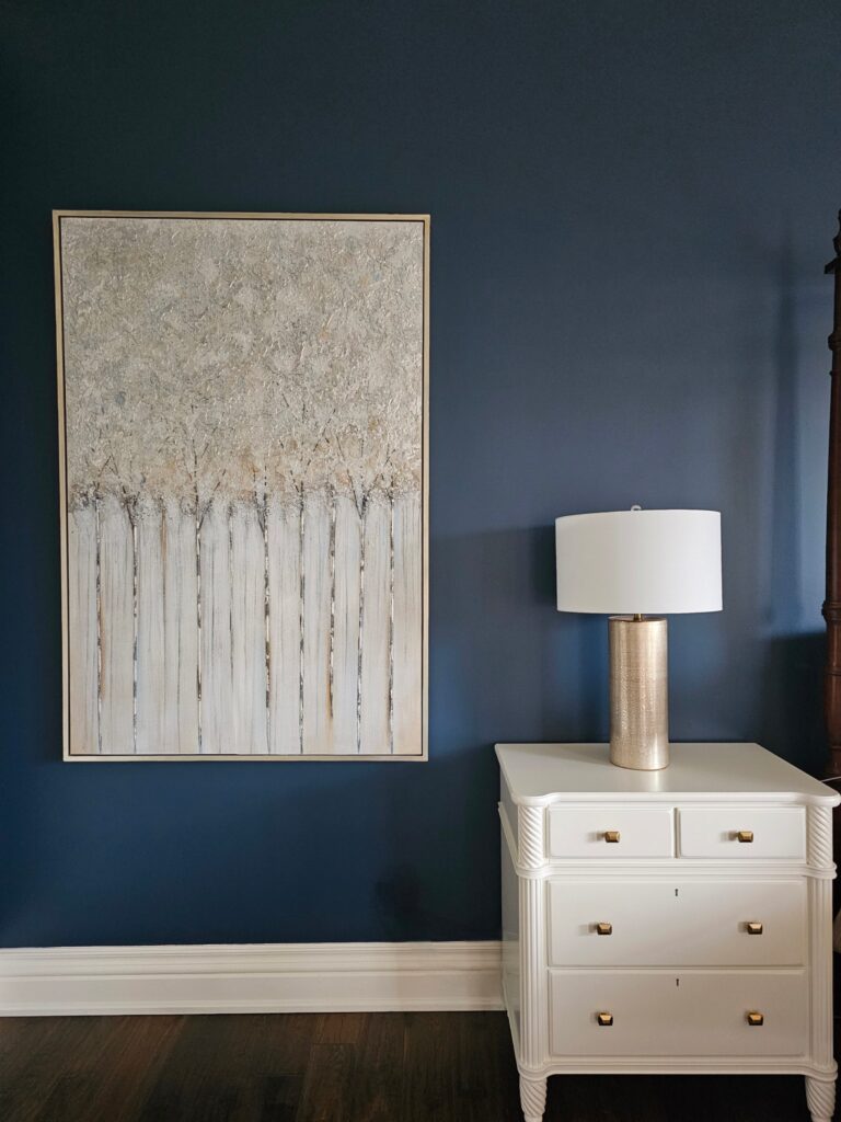 After photo of white painted nightstand with gold hardware and textured tree artwork on Hale Navy, part of moody bedroom makeover by clairejefford.